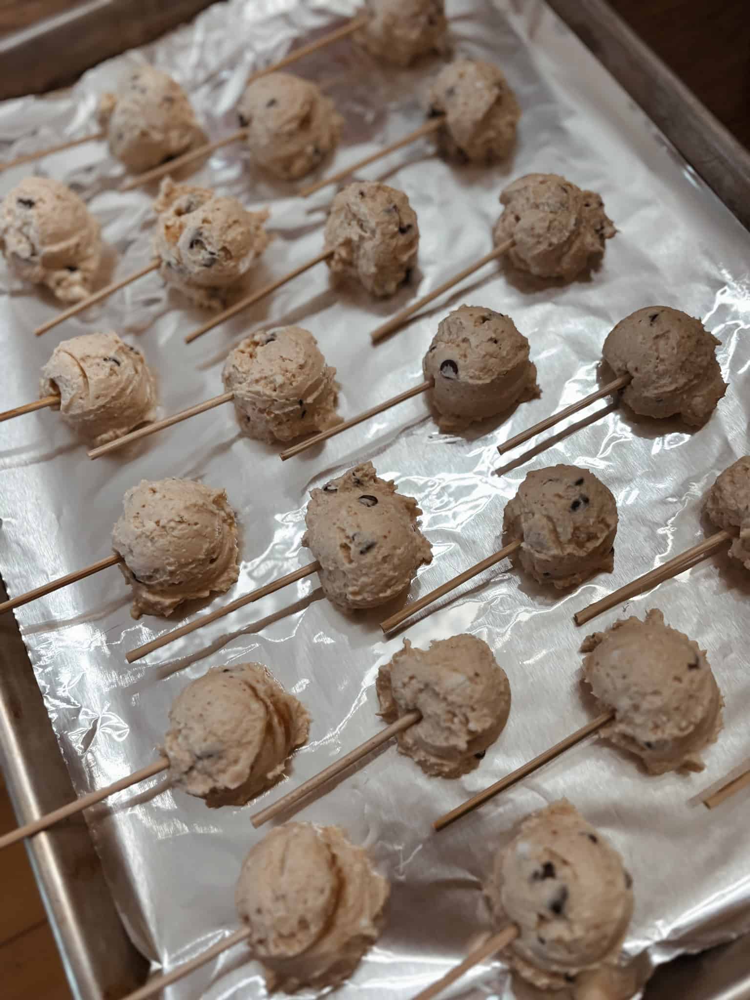 Mini frozen yogurt balls on cookie sheet with sticks inserted