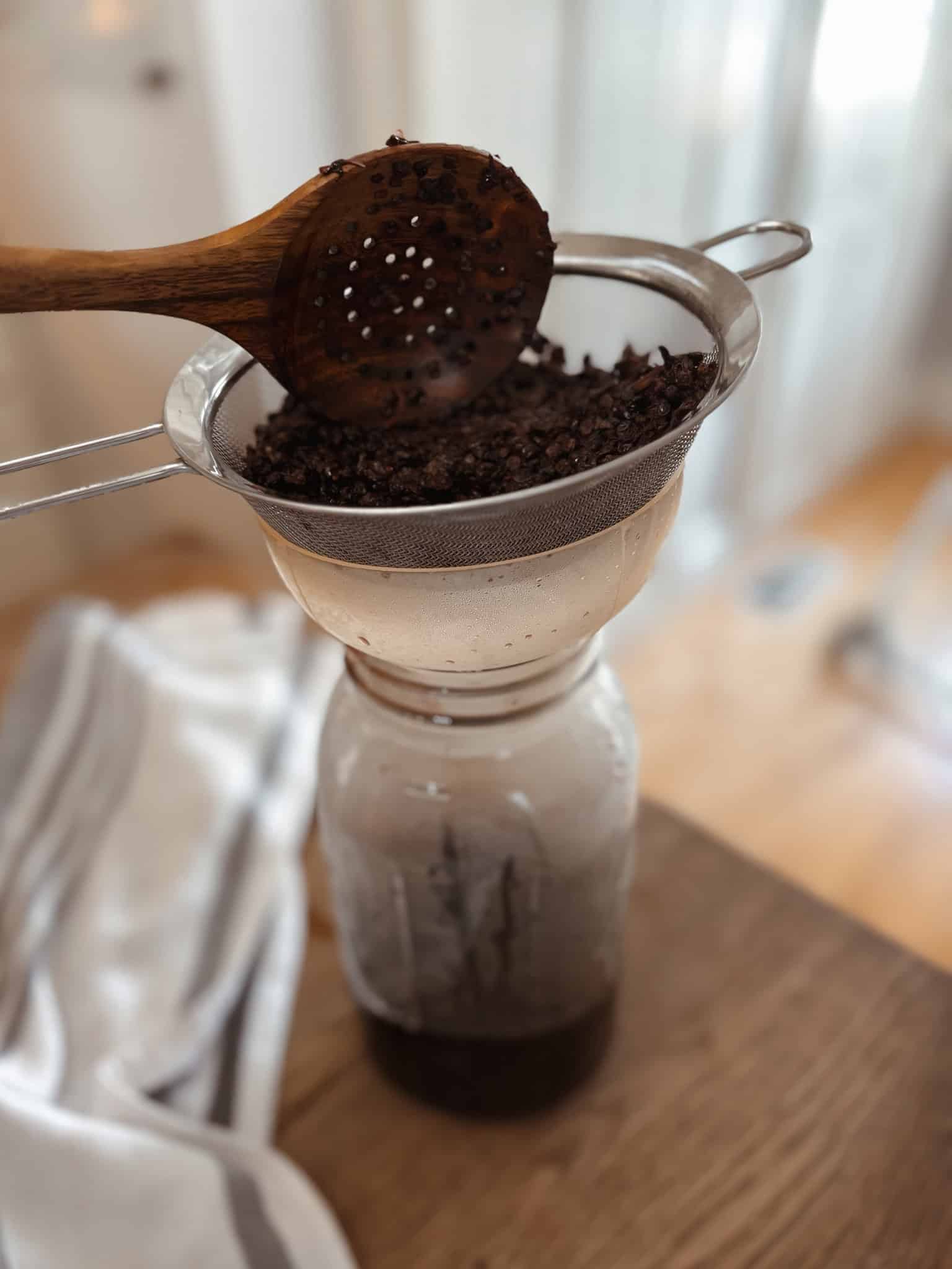 Homemade elderberry honey syrup for a natural immune support step two straining in colander 