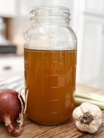 Featured image for homemade bone broth in a mason jar next to onion, garlic, and celery