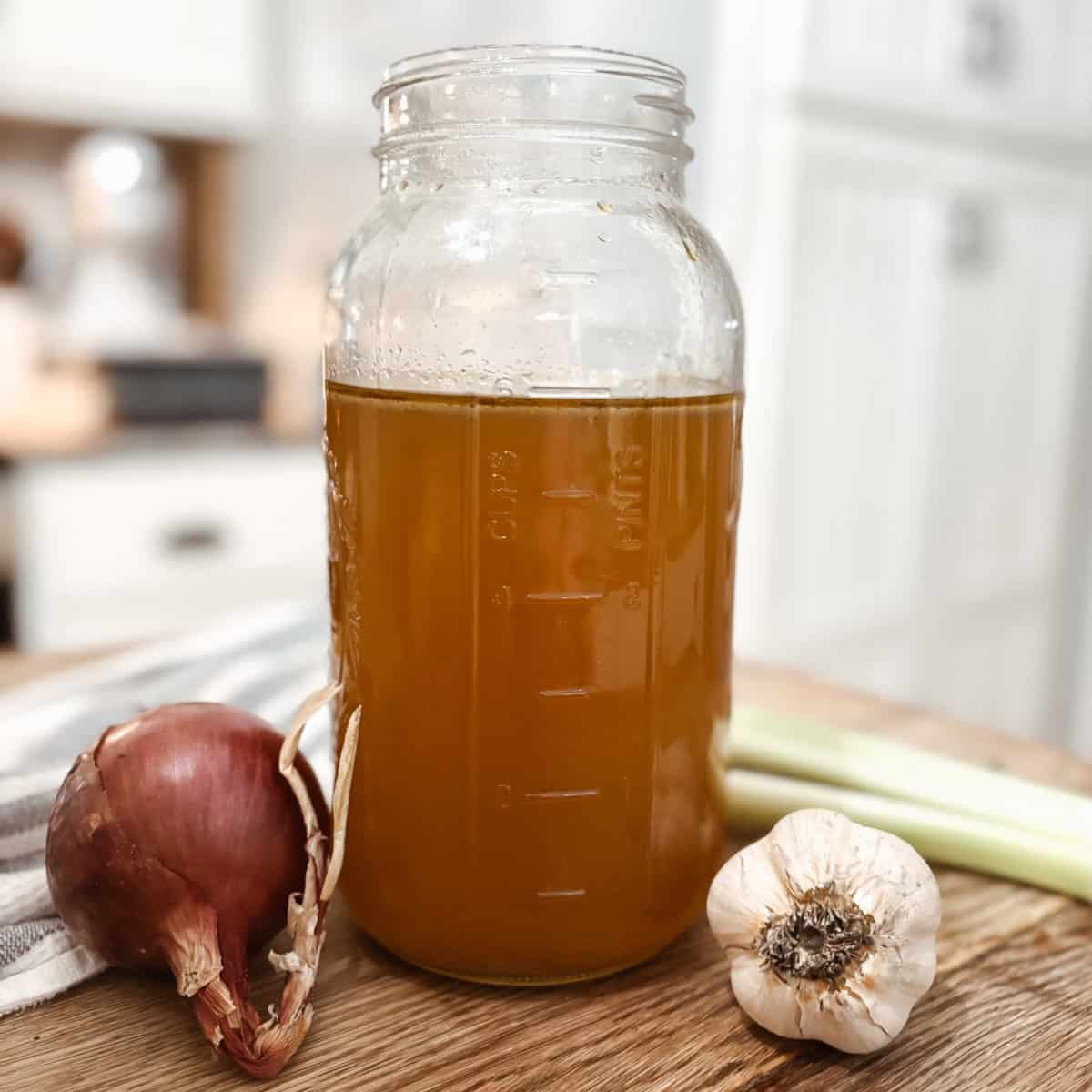 Featured image for homemade bone broth in a mason jar next to onion, garlic, and celery