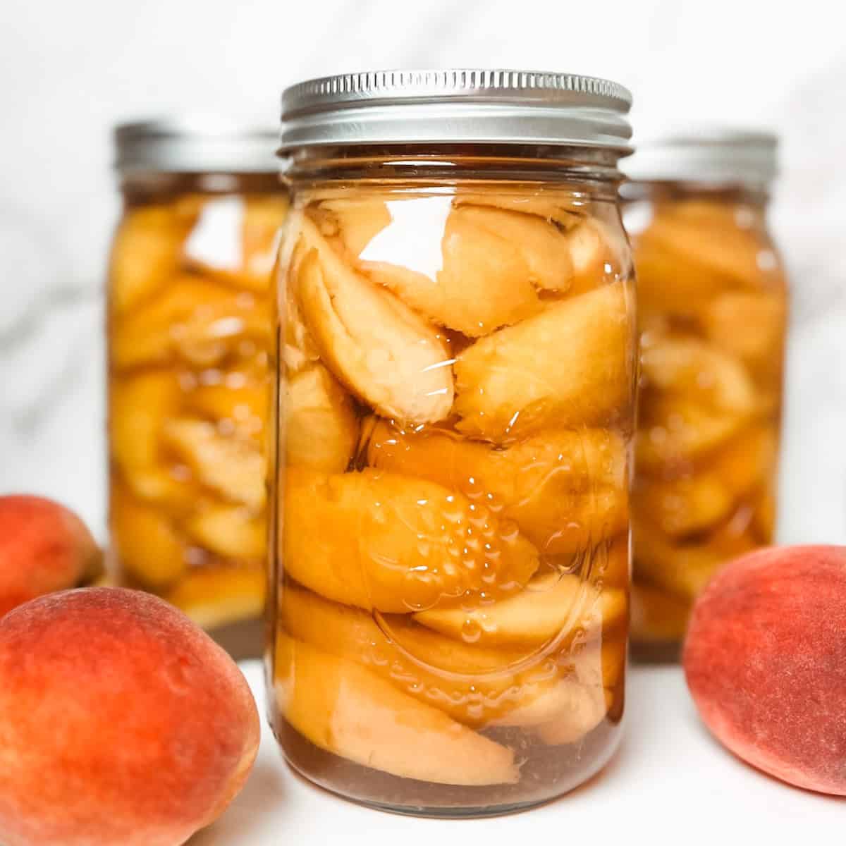 featured image of pretty canned peaches in jars with some fresh peaches